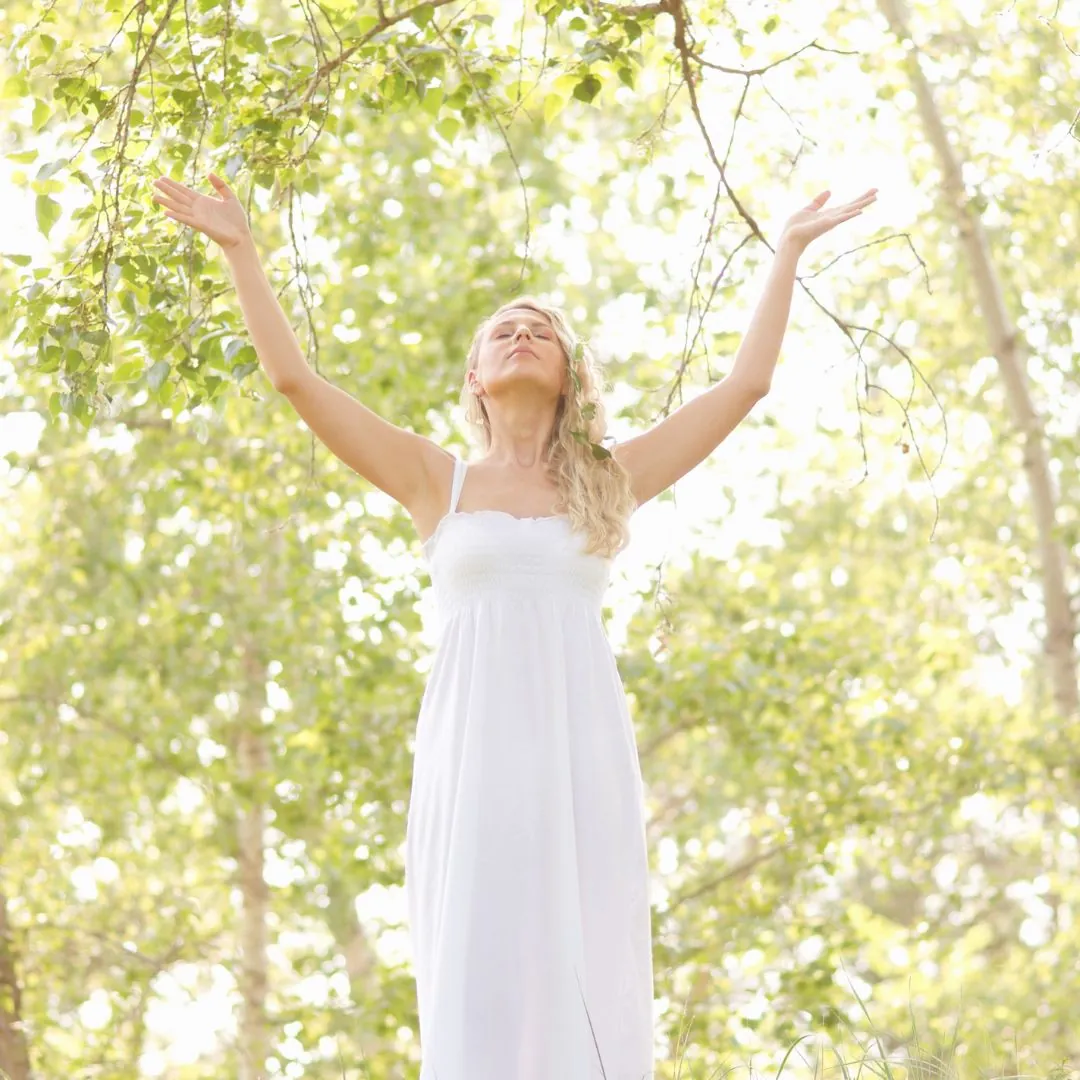 Donna nella natura, che alza le braccia al cielo, a simboleggiare l'elevazione spirituale, la connessione con l'universo e il potere del femminile sacro