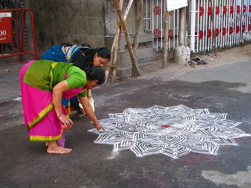 Deux femmes indiennes montrant un Kolam mandala dessiné sur le sol, représentant l'art traditionnel et la culture spirituelle indienne