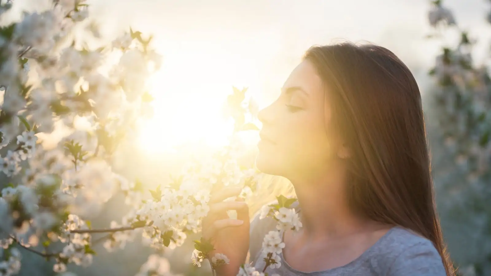 Frau atmet den süßen Duft von Blumen ein, symbolisiert die Verbindung mit der Natur und die Aktivierung der Kraft der Absicht
