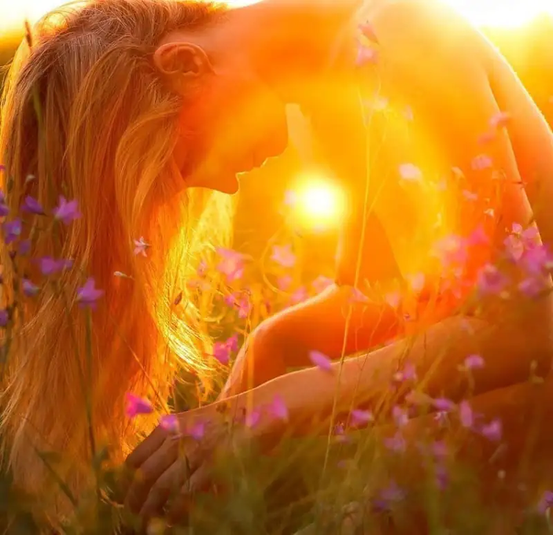 Woman in nature at sunset, surrounded by flowers, symbol of harmony, gratitude, and vibrational elevation