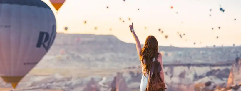 Many hot air balloons in the sky with a woman pointing her finger at the sky, symbolizing elevation, freedom, and the search for lightness in life